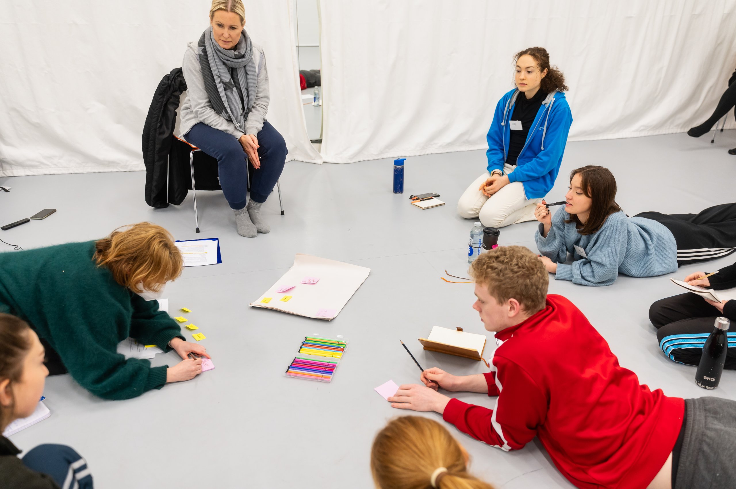 A group of people are sitting, kneeling or laying down in a circle, drawing and writing. 