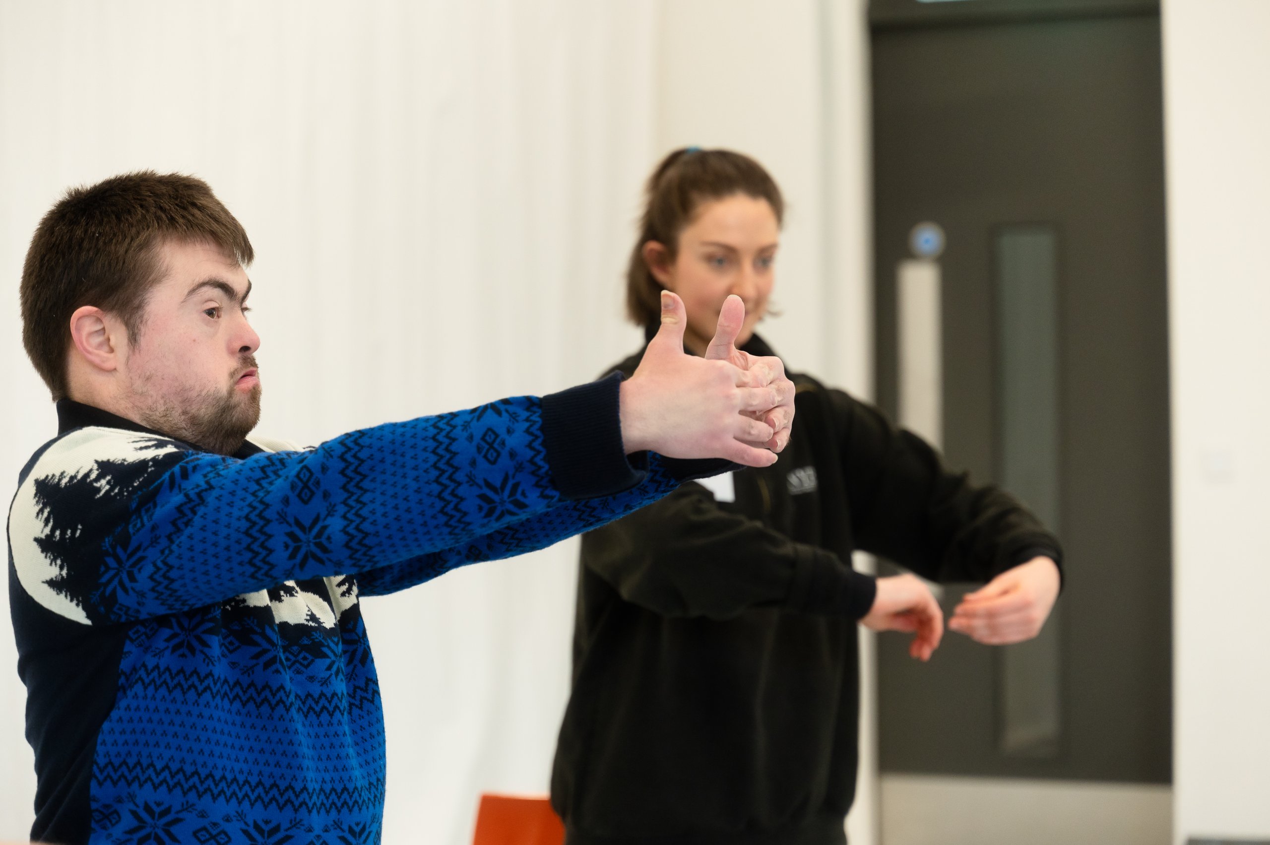 Two dancers with arms in a rounded position in front of them. 