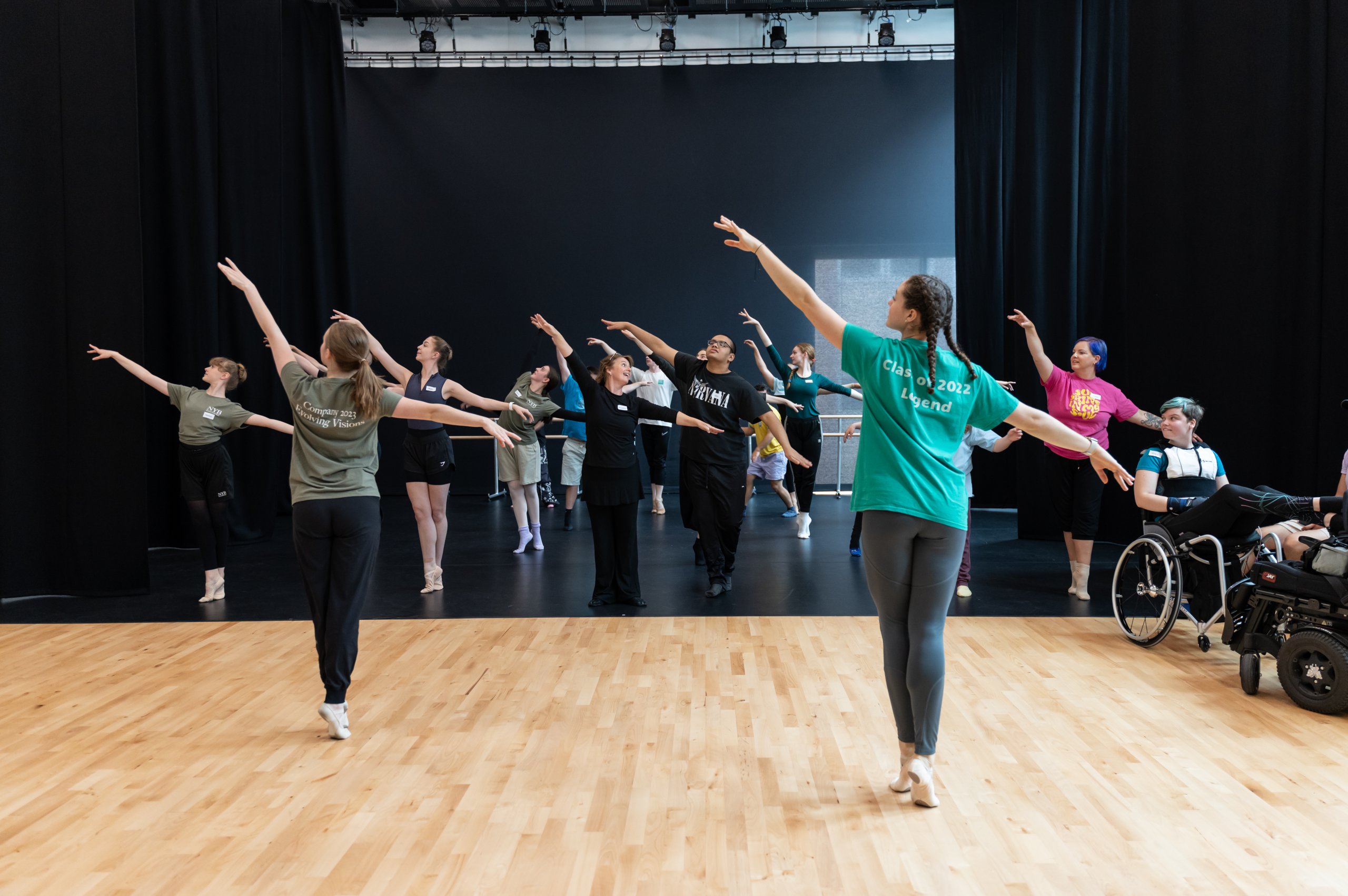 The whole company of dancers reach wide with their upper body or arms whilst looking up to the corner. 