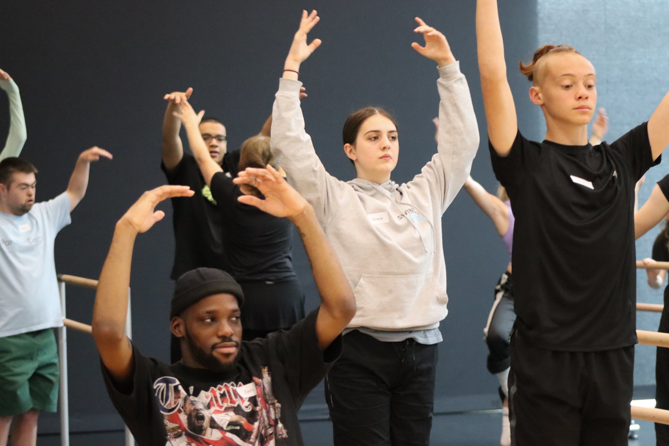 Dancers placed at different levels with their arms in fifth positions facing forwards. 