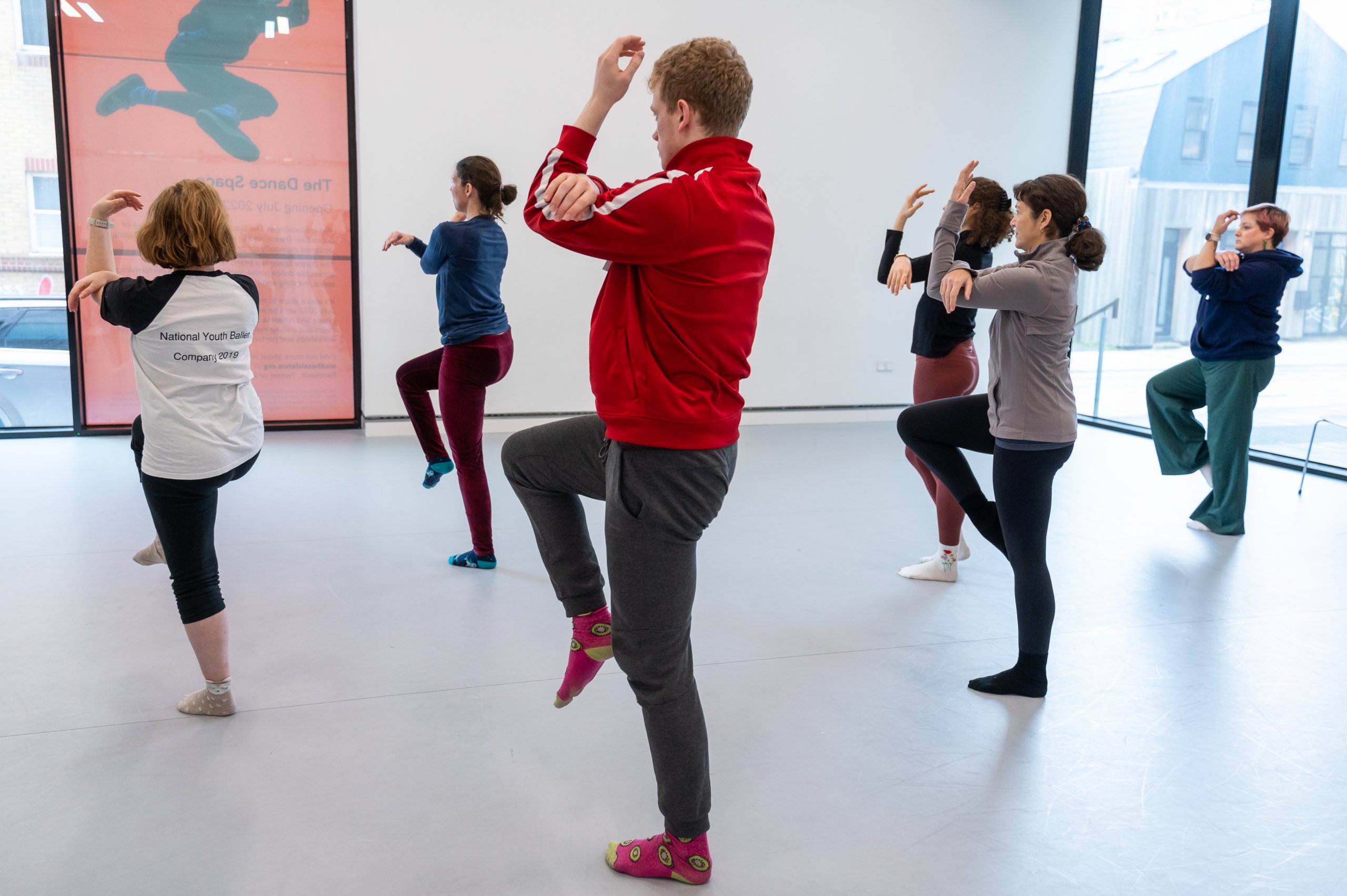 Six dancers standing on one leg with one arm folded over the other. 