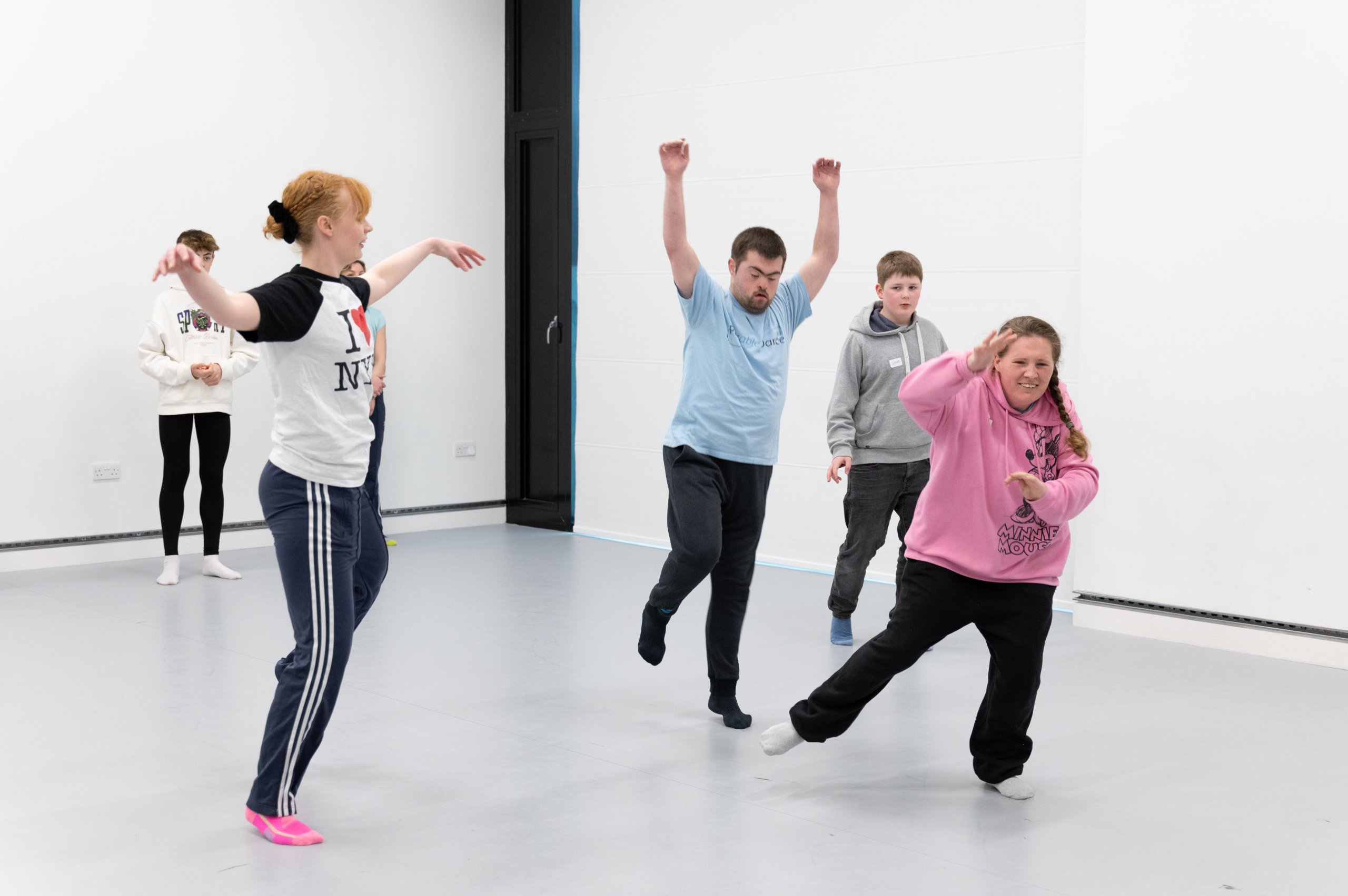 Five dancers in motion in different ways, each dancer has their arms reaching high, middle or low and some dancers are balancing on one leg. 