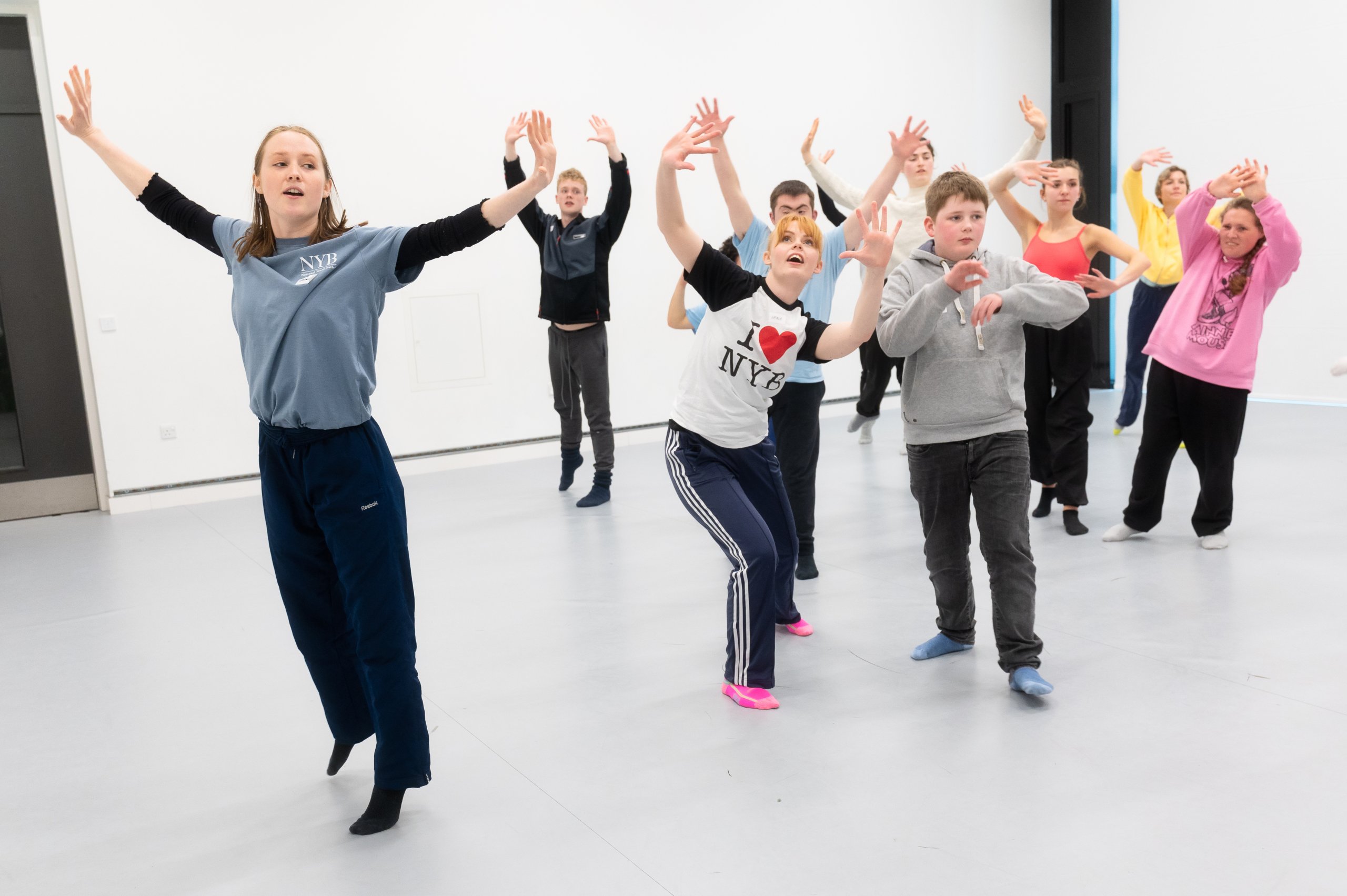 A large group of dancers with arms raised in the air above their heads. 
