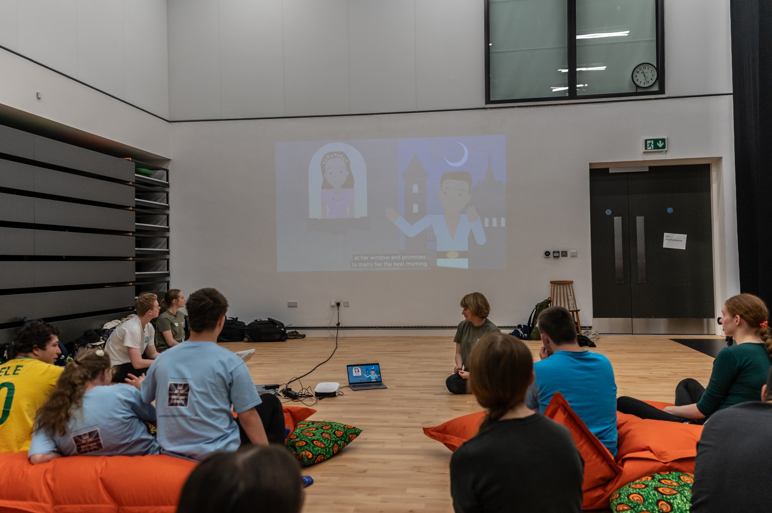 Many people sit on beanbags whilst looking at a projection on the wall which is displaying an animation. 