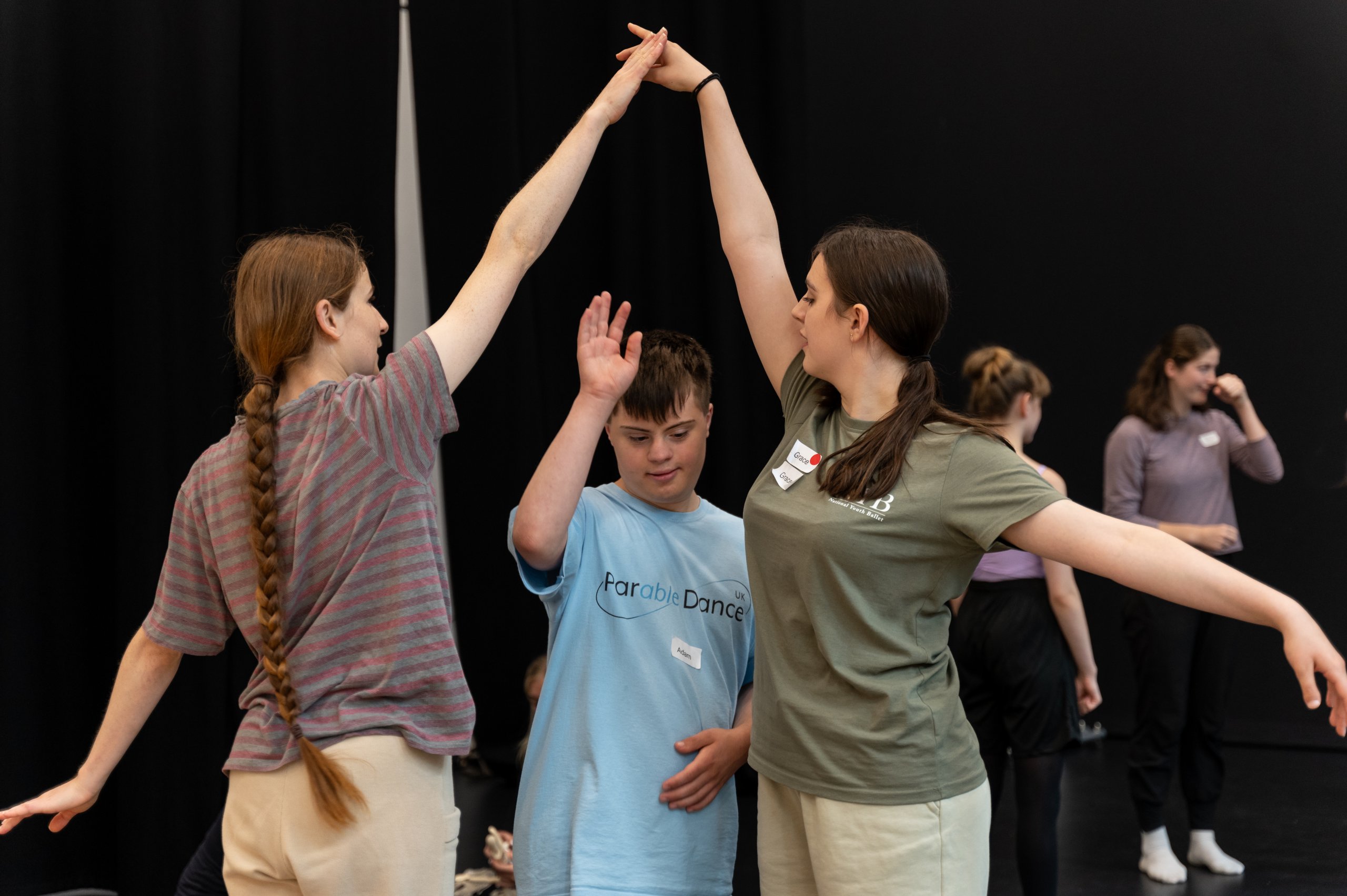 Two dancers join their hands over their head whilst another dancer steps through. 