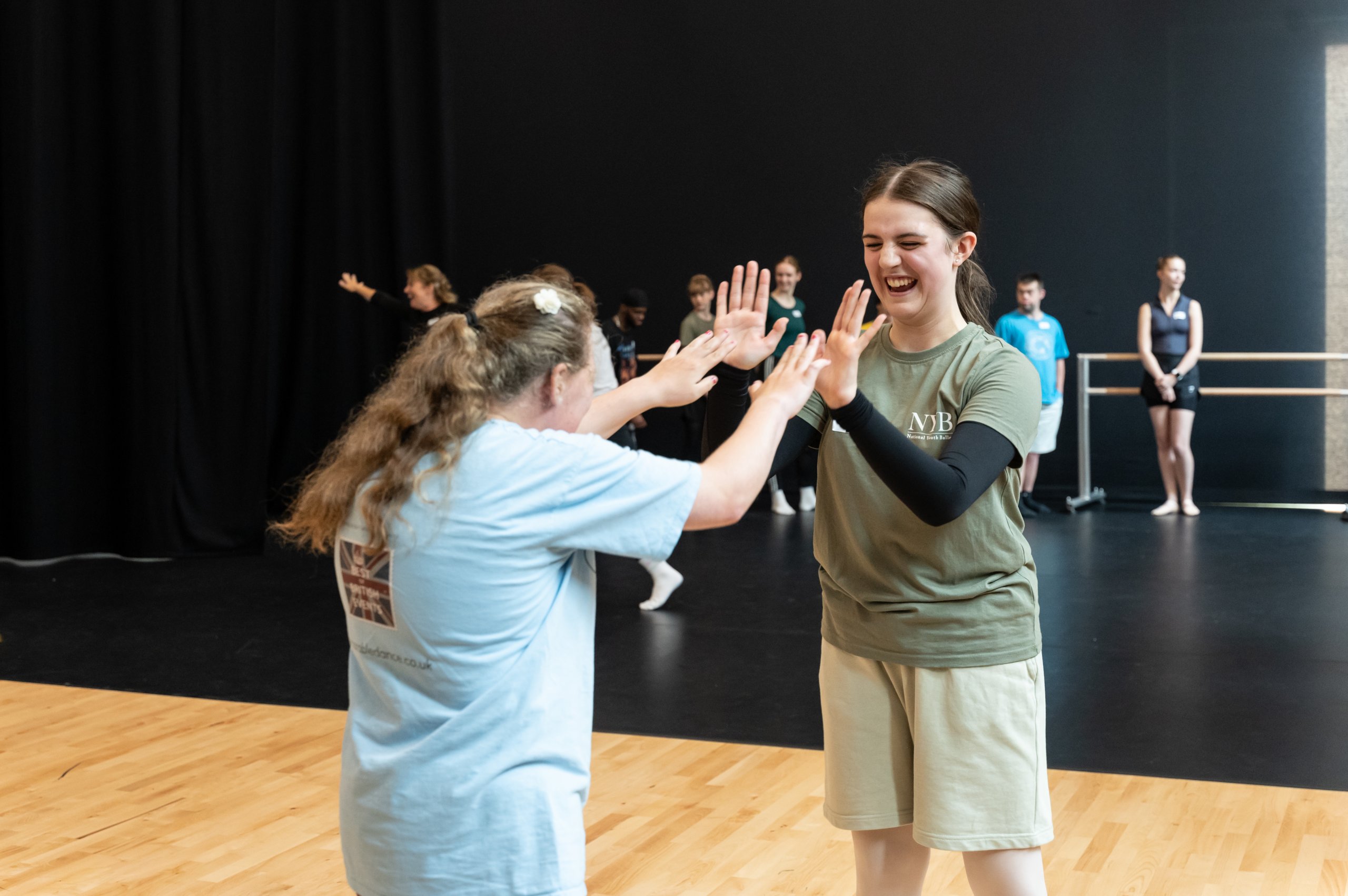 Two dancers smiling and facing each other about to touch both palms with each other. 