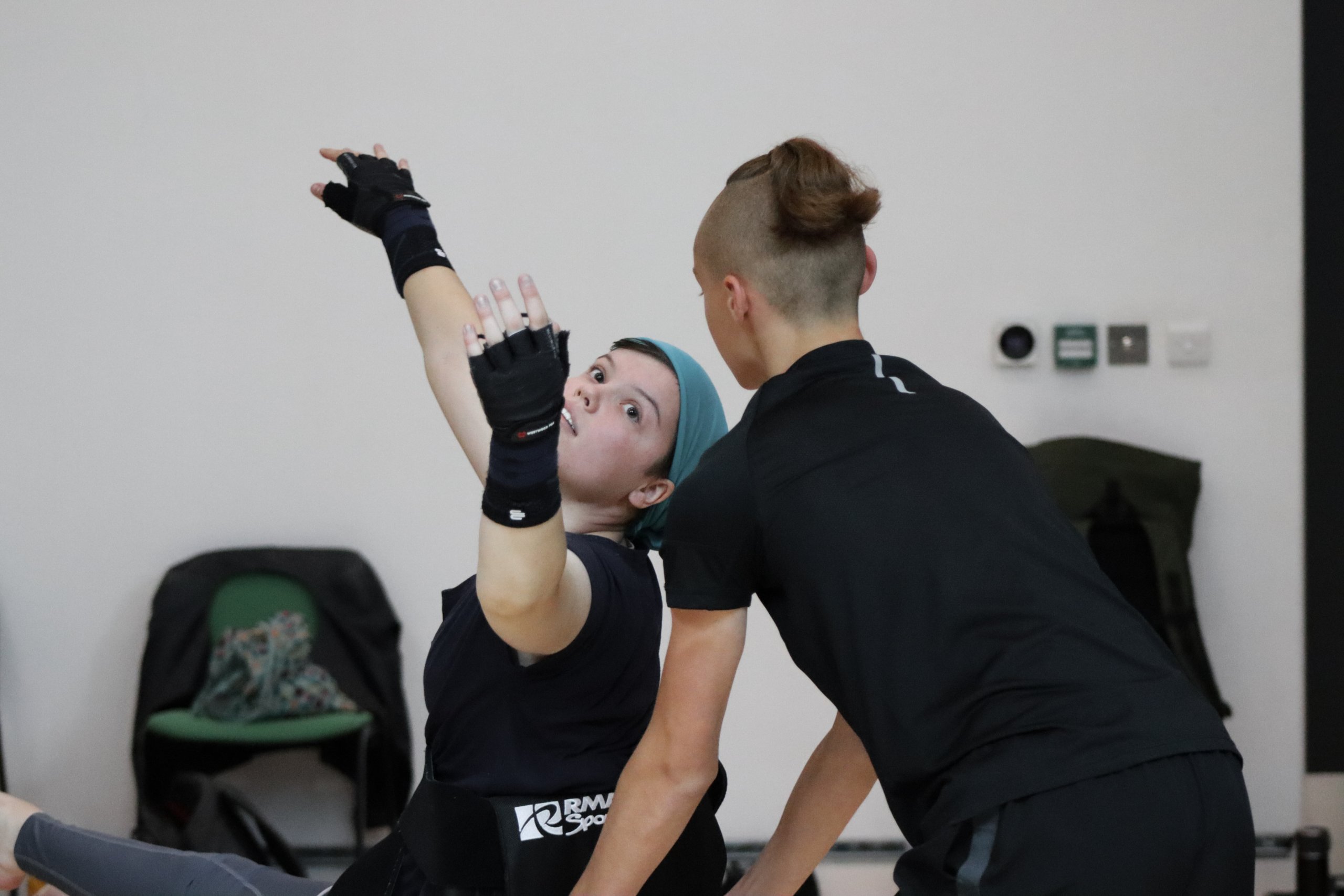 A dancer gesturing backwards whilst looking at another dancer. 