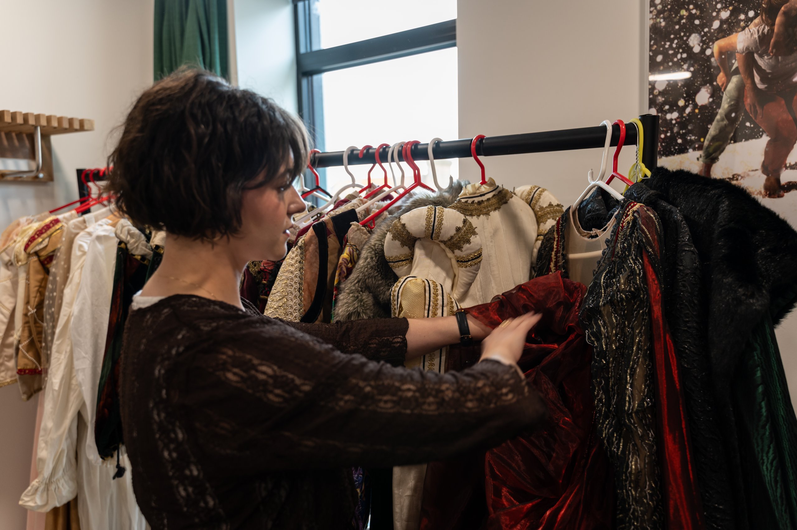 Person next to a rail of costumes, touching one of the costumes. 