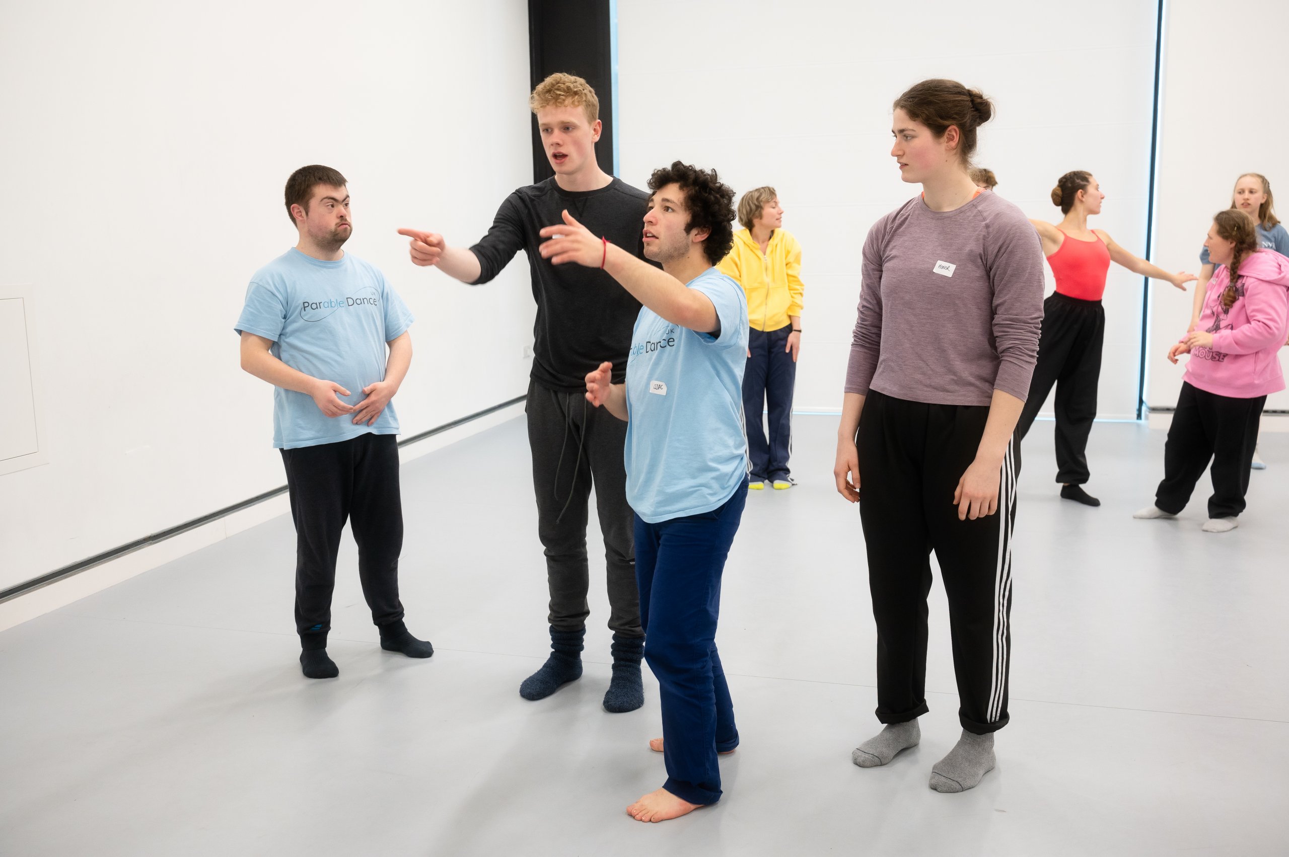 A group of four dancers stand together. Two are pointing forwards and the other two are observing this. 