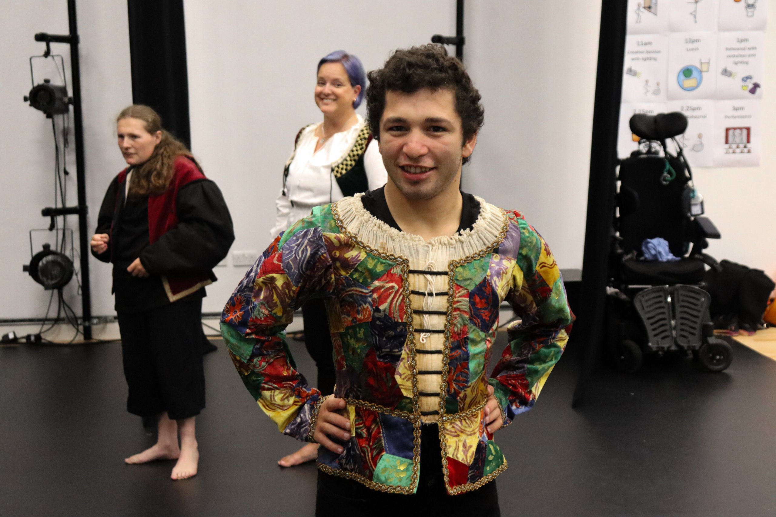 A dancer in their costume with their hands placed on hips. Two dancers are in the background also in costume. 