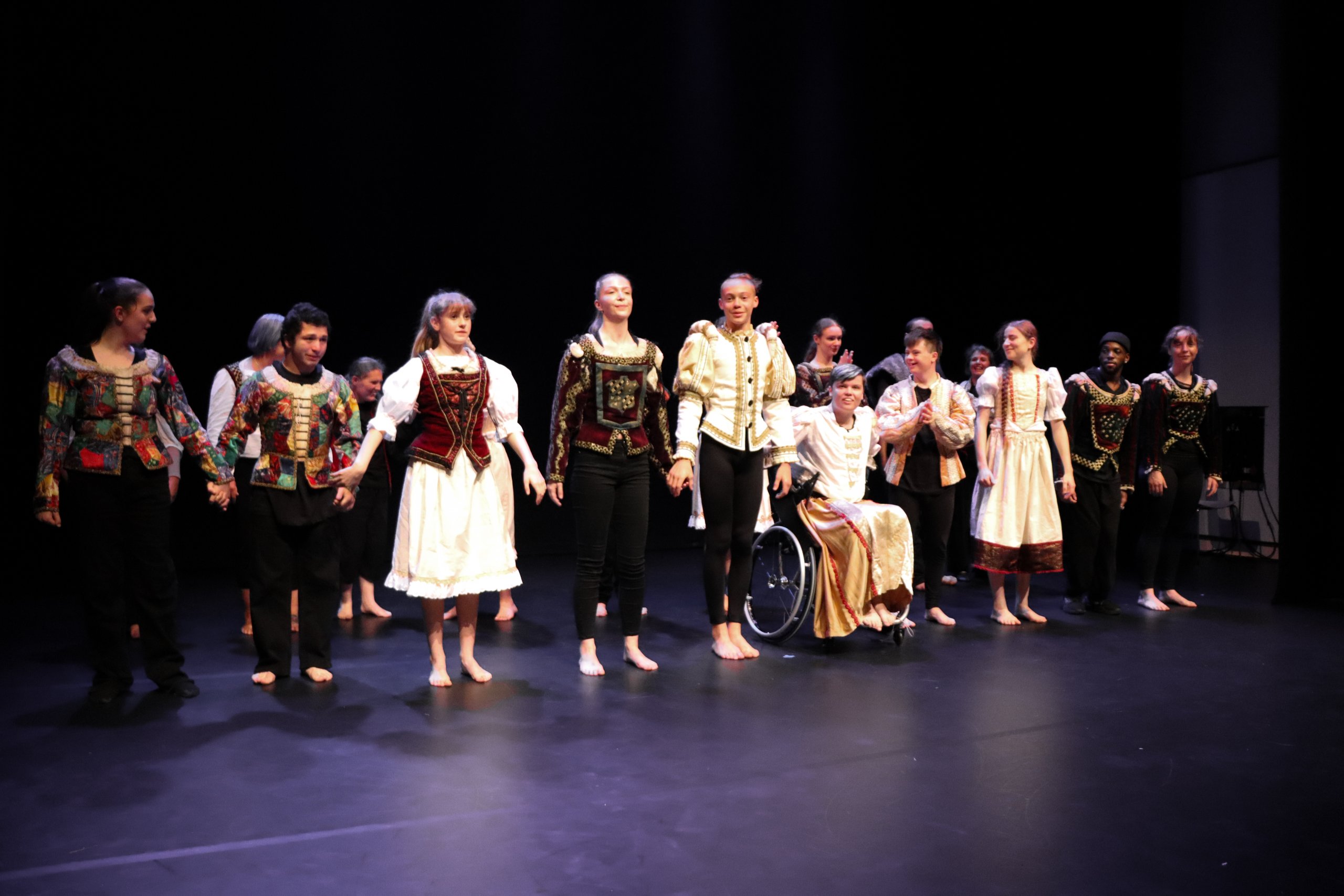 Dancers lined up side by side holding hands on stage and in costume. 
